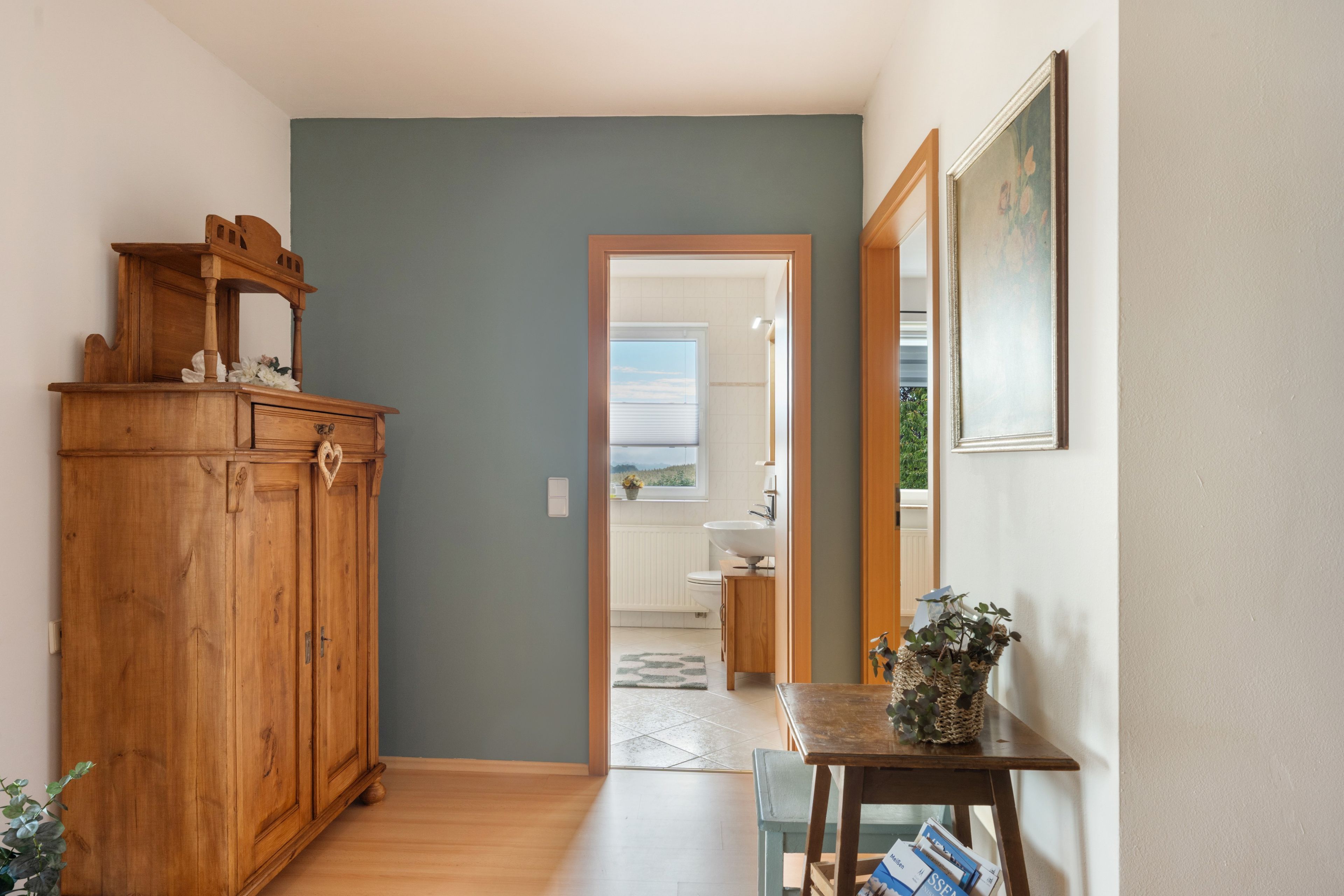 A hallway with a wooden cabinet, a table with magazines, and a door leading to a bathroom.
