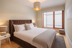 A bedroom with a large bed, bedside lamps, a window with blinds, and a hanging light fixture. - Virginie Almada Apartment (Porto)