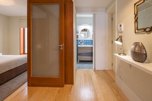 Ett hotellrum med en trädörr, en säng, ett badrum med spegel och handfat samt ett litet bord med en lampa och en vas.