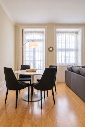 A dining area with a round table, four chairs, a floor lamp, and a window with sheer curtains. - Virginie Almada Apartment (Porto)