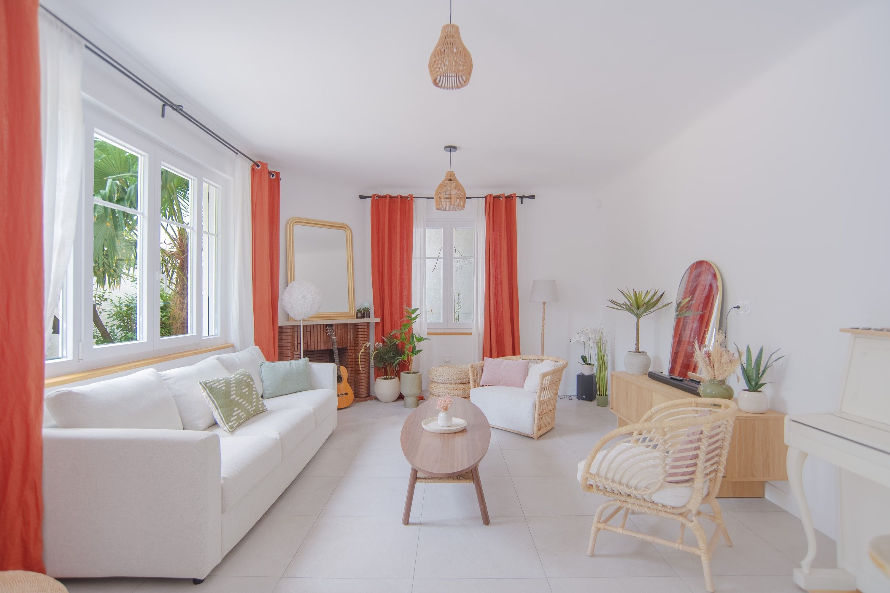 A bright living room with a white sofa, a wicker chair, a small round table, and a fireplace.