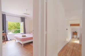 A bedroom with a bed, a bedside table, a window with curtains, and a view of greenery outside. - Villa Campbell - entre Biarritz et Bayonne (Anglet)
