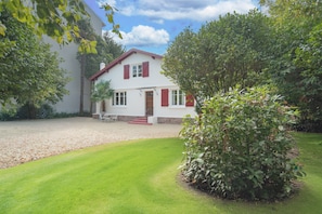 Ein zweistöckiges Haus mit weißer Fassade und roten Fensterläden, einer Schotterauffahrt und einem gepflegten Rasen.