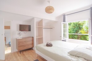 Ein Schlafzimmer mit Bett, Kommode, Fernseher und einem Fenster mit Blick auf Grünflächen.