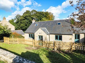 A stone cottage with a wooden fence, a stone pathway, and a grassy lawn. - Stone Lily Cottage (Buxton)