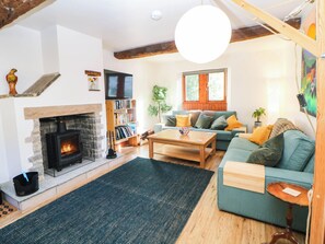 A cozy living room with a fireplace, a sofa, a coffee table, and a bookshelf. - Stone Lily Cottage (Buxton)