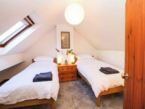 A bedroom with two beds, a skylight, a bedside table with a lamp, and a framed picture on the wall. - Stone Lily Cottage (Buxton)