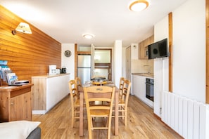 A compact kitchen with wooden cabinets, a dining table with chairs, a built-in microwave, and a television mounted on the wall. - DFJ Des Neiges - station de ski accessible à pied (Chamrousse)