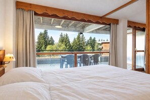 A bedroom with a large bed, a balcony with chairs, and a view of trees. - DFJ Des Neiges - station de ski accessible à pied (Chamrousse)