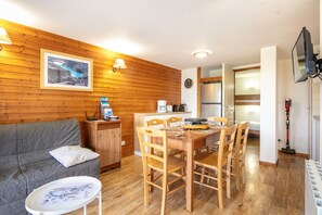 Quarto aconchegante com parede de madeira, uma mesa de jantar com cadeiras, um sofá, uma pequena mesa com um mapa e uma TV na parede.