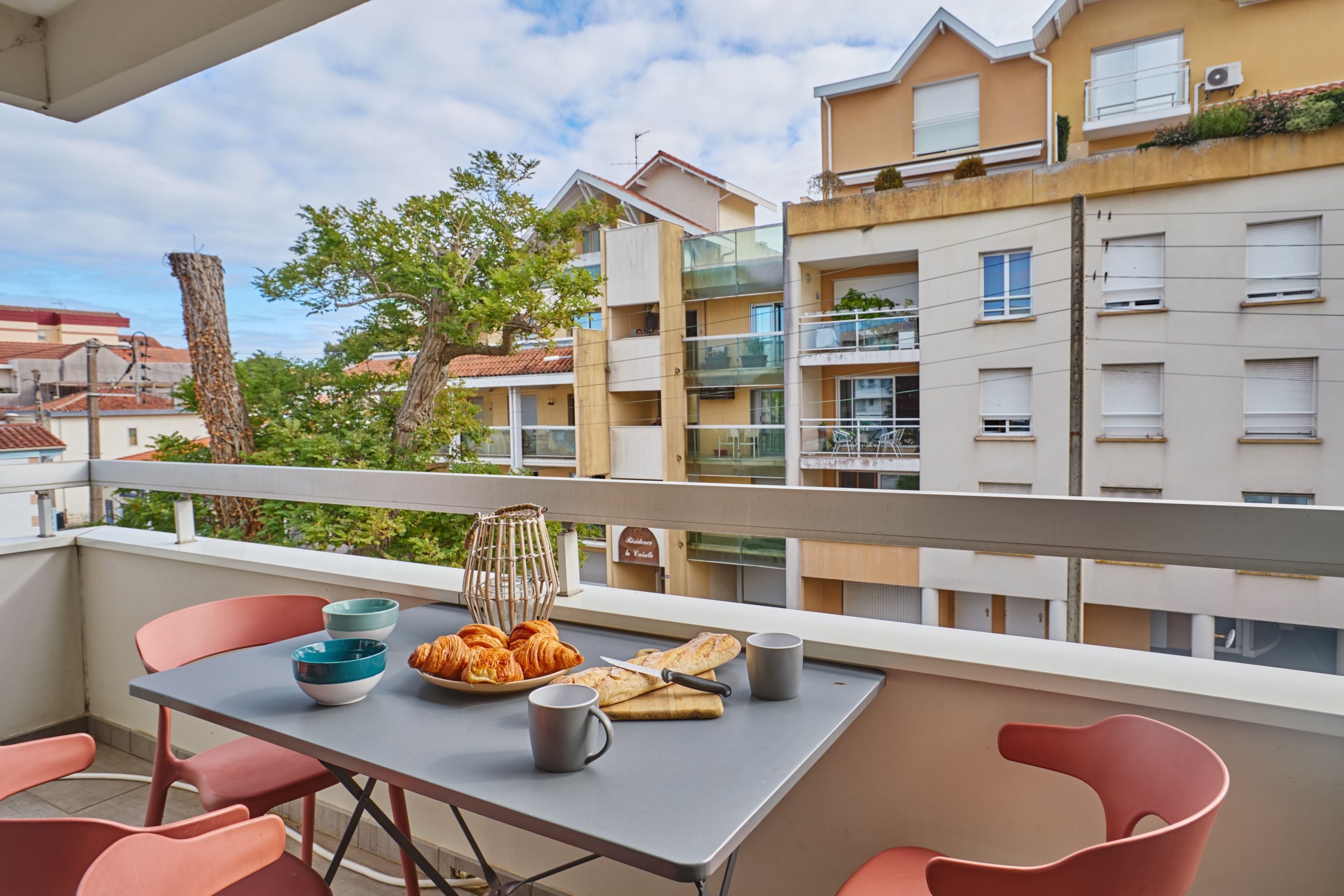A balcony with a table set for breakfast, including croissants and a mug.