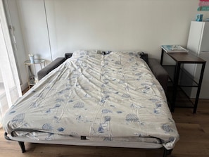 A bed with a patterned bedspread, a small bedside table, a chair, and a desk with a chair. - L'écrin d'Arcachon - proche des plages (Arcachon)