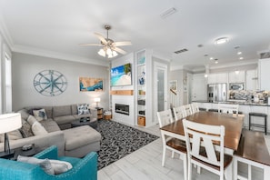 A modern living room with a fireplace, a dining area with a wooden table, and a kitchen with white cabinets. - Mexico Beach Best Pool | Karaoke Loft | Canal View (Mexico Beach)