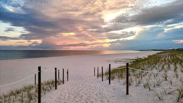 A beach with a sandy path leading to the water, surrounded by dunes and a rope barrier.