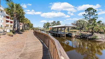 A wooden boardwalk leading to a dock area with a covered structure, surrounded by palm trees and a clear sky.