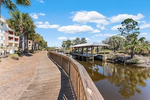 A wooden boardwalk leading to a dock area with a covered structure, surrounded by palm trees and a clear sky. - Mexico Beach Best Pool | Karaoke Loft | Canal View (Mexico Beach)