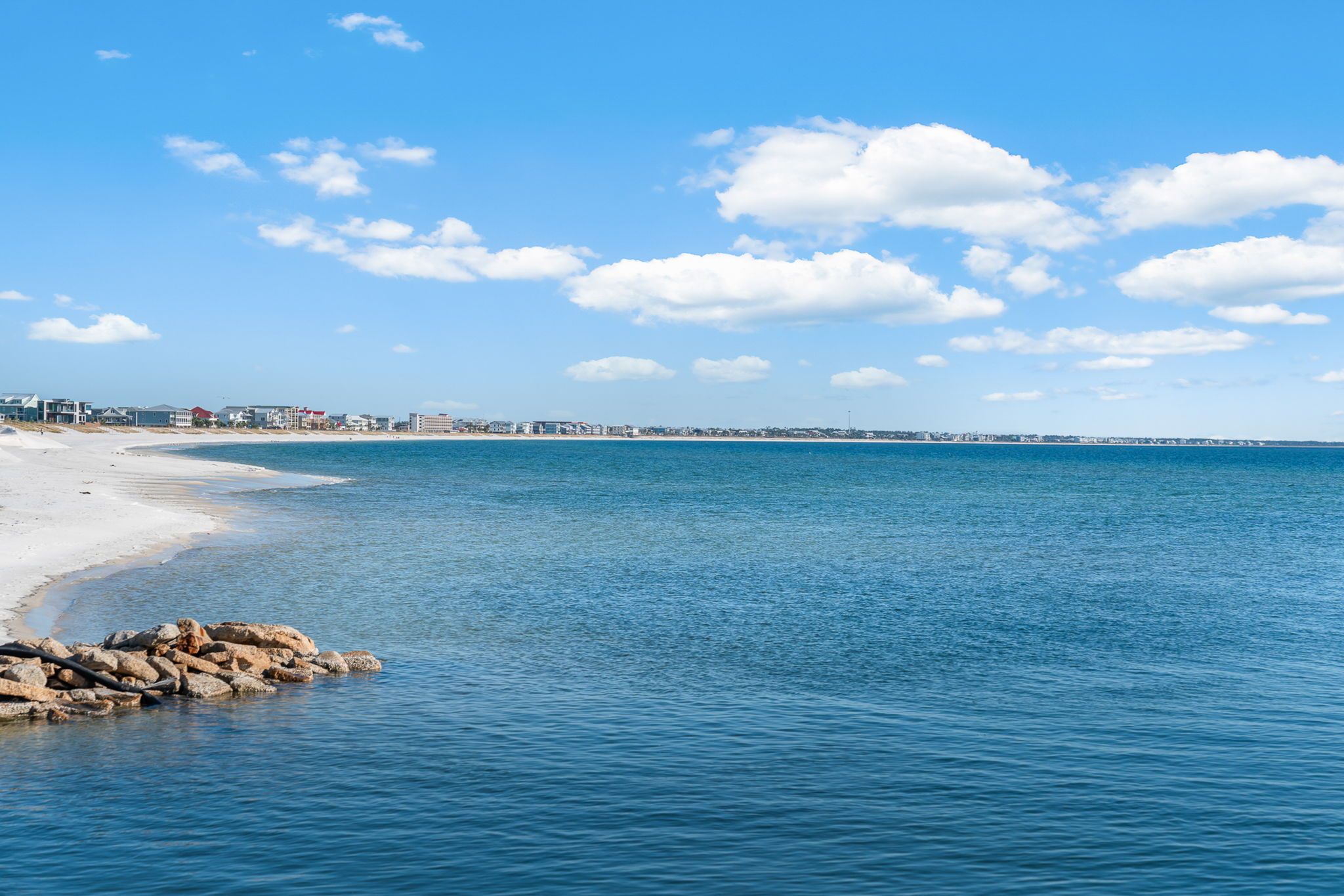 Une scène de plage côtière, avec un ciel dégagé, une mer calme et une côte rocheuse.