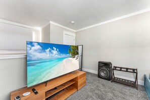 A flat-screen TV on a wooden stand, a black speaker, and a wooden rack with shelves.