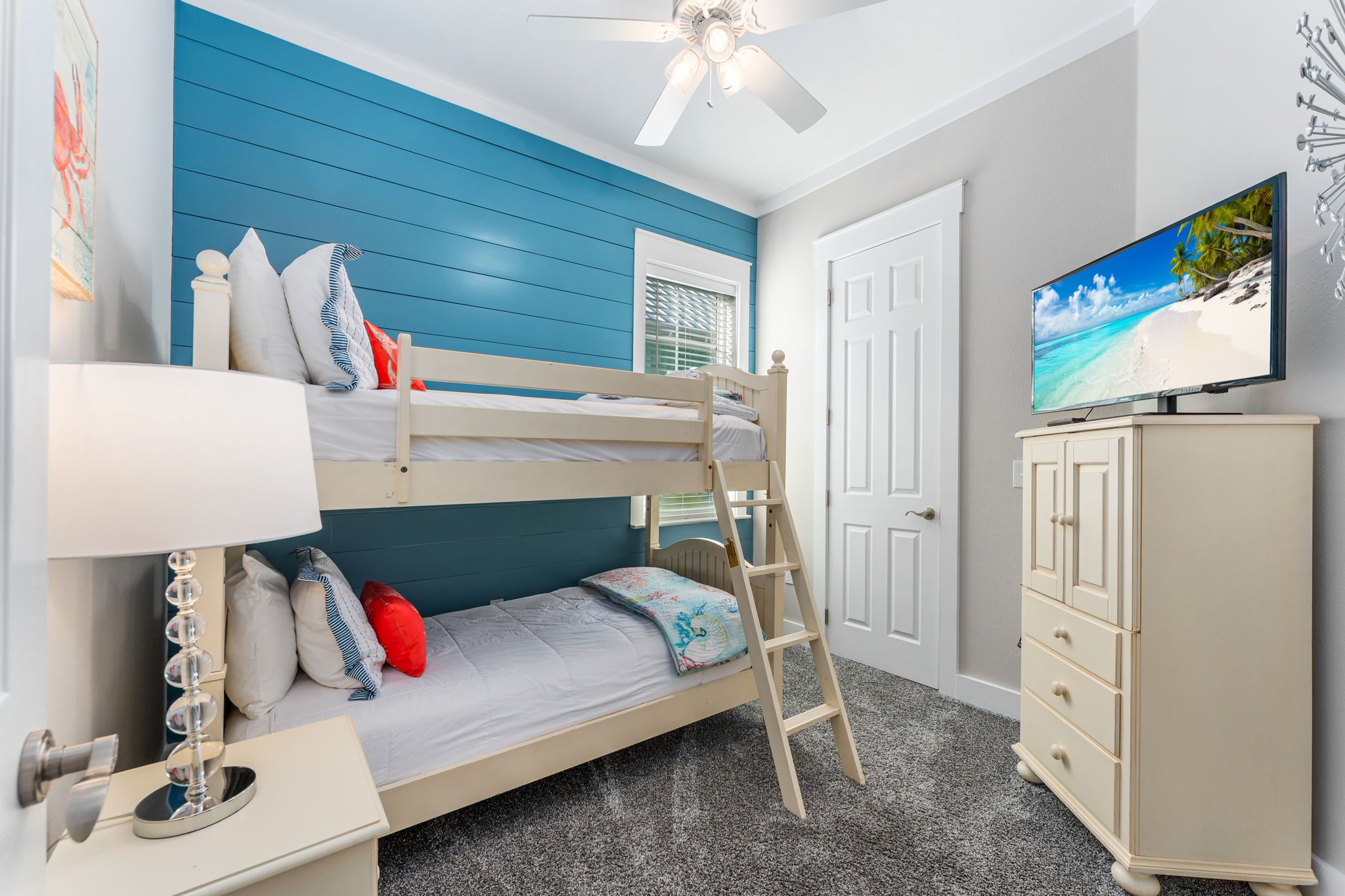 A bunk bed with a ladder, a television on a cabinet, and a ceiling fan.