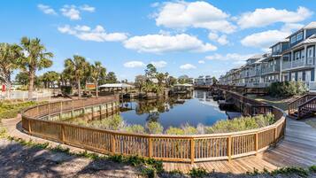 A waterfront property with a wooden deck, a calm lake, and a row of multi-story buildings.