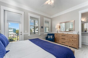 A bedroom with a bed, dresser, mirror, and windows.