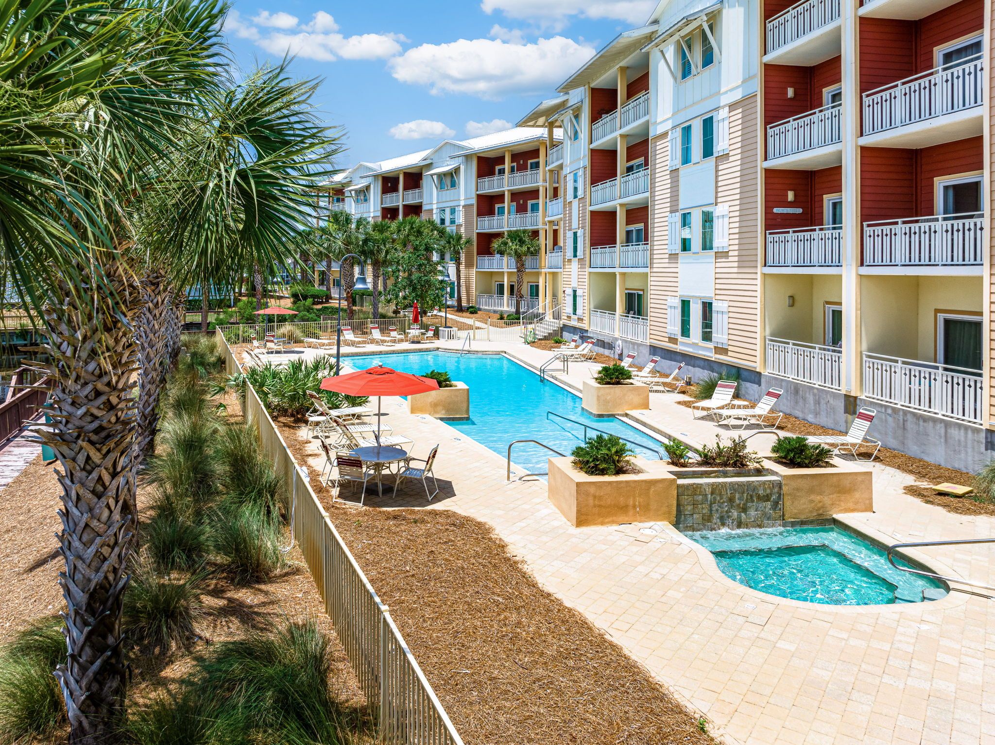 A resort with a swimming pool, lounge chairs, and palm trees.