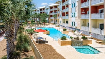 A resort with a swimming pool, lounge chairs, and palm trees.