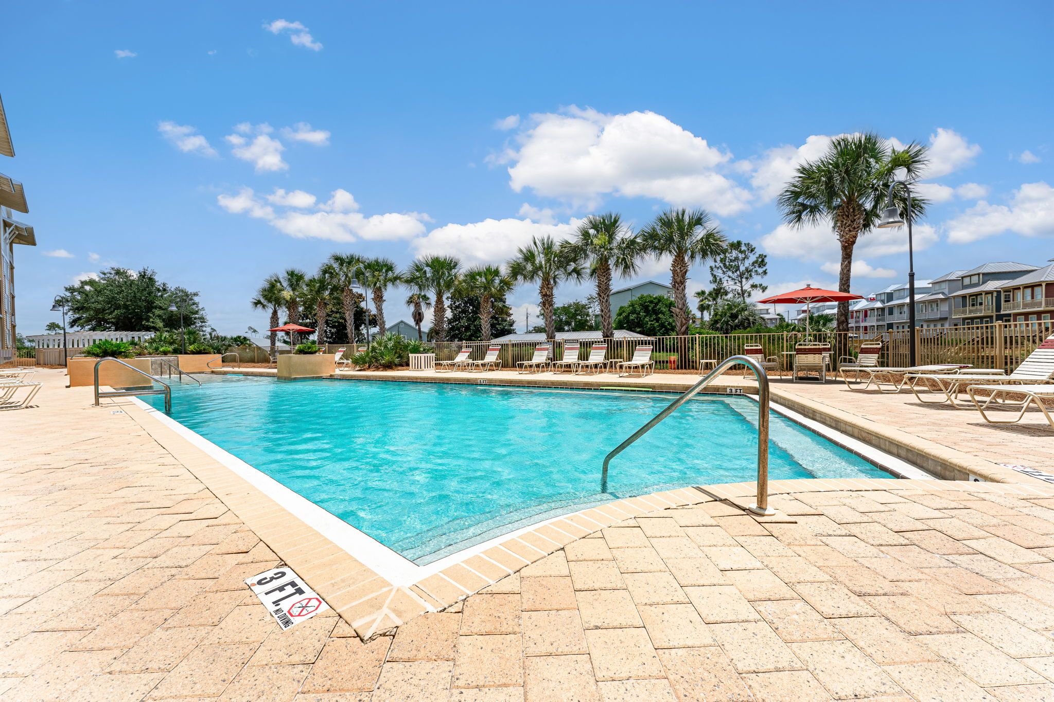 Une piscine avec un panneau indiquant une profondeur minimale de 3 pieds pour la plongée, entourée de palmiers et de chaises longues.