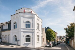 Een wit gebouw met gebogen ramen en een plat dak, gelegen aan een straat met geparkeerde auto's en een heldere lucht.