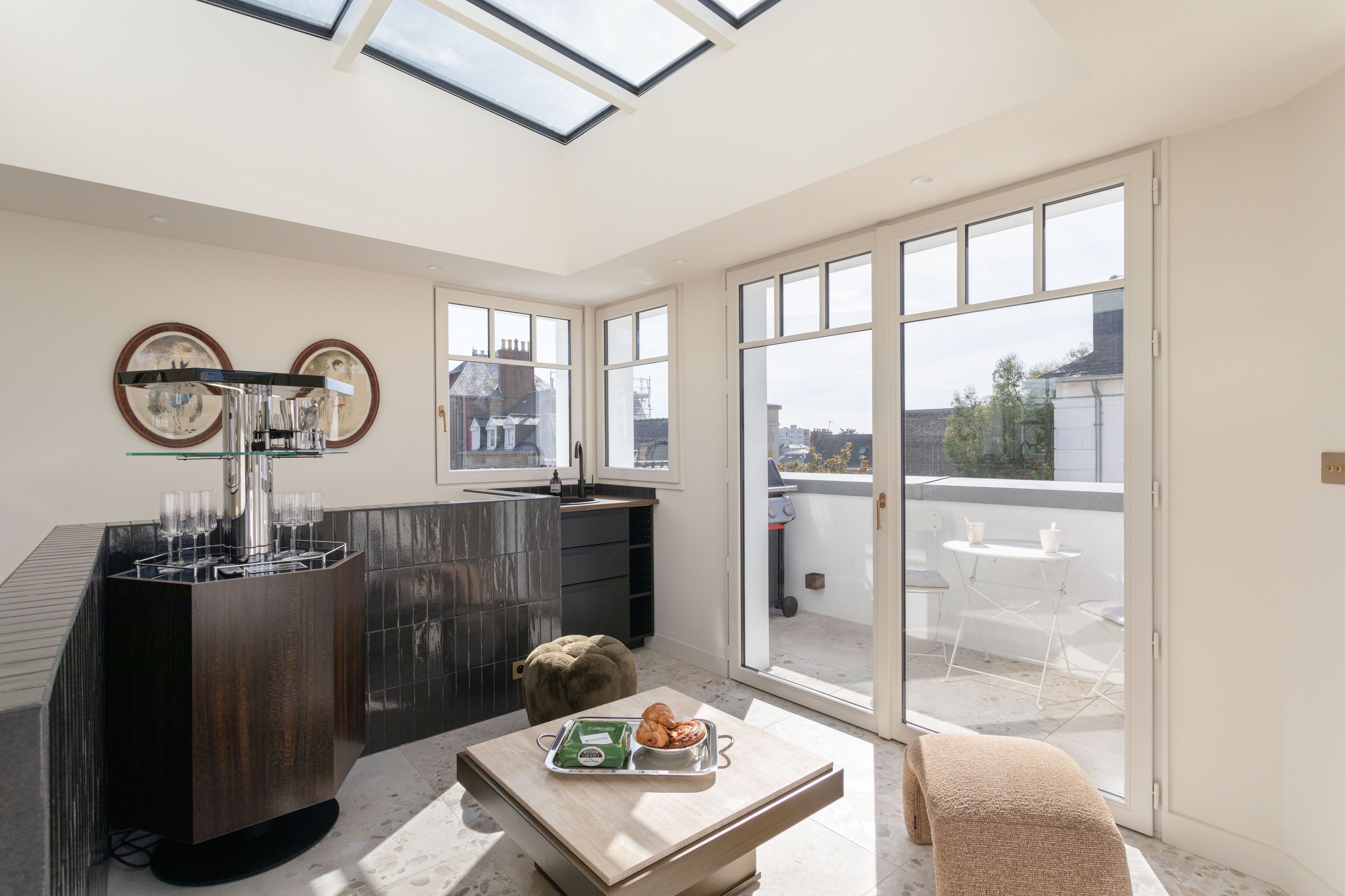 Una cocina moderna con una máquina de espresso integrada, un comedor con mesa y sillas, y amplios ventanales con vistas a la ciudad.