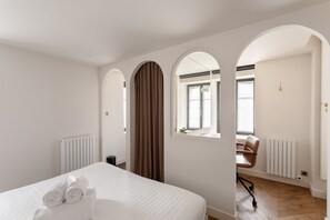 Een slaapkamer met een bed, een radiator, een raam en een boogvormige deuropening.