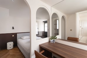 Ein Hotelzimmer mit einem Bett, einem Holztisch, einem Stuhl, einem Mülleimer und einem Spiegel.