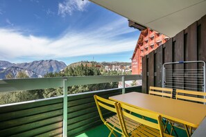 A balcony with a table and chairs, overlooking a mountainous landscape and a building with balconies. - L’écrin 206 - Quartier des Bergers - Proximité immédiate ESF (Huez)