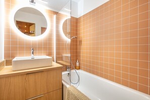 A modern bathroom with a white sink, wooden vanity, and a bathtub. - L’écrin 206 - Quartier des Bergers - Proximité immédiate ESF (Huez)