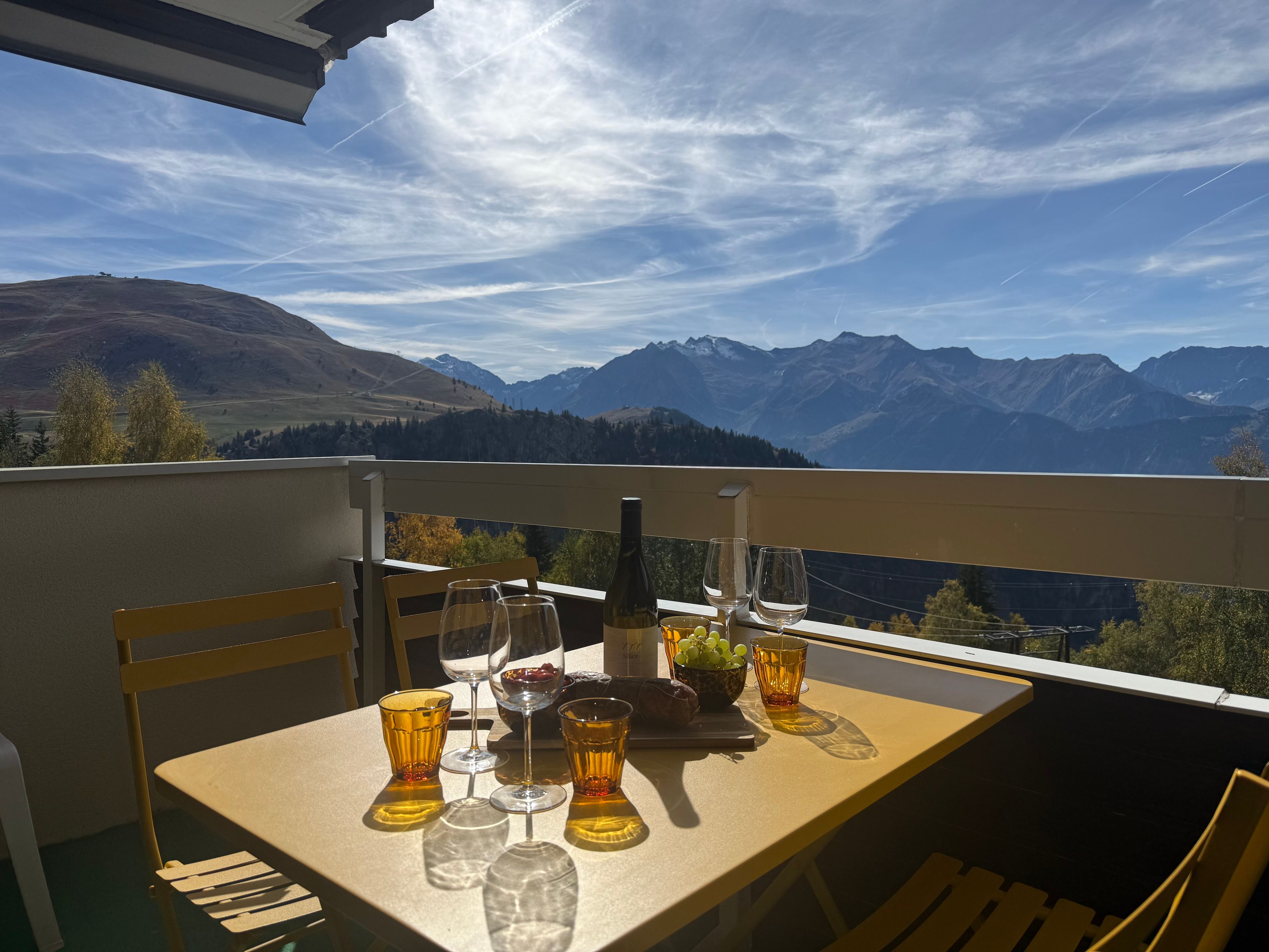 A table set for two with glasses and a bottle, overlooking a mountainous landscape.