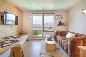 Ett modernt vardagsrum med en soffa, ett soffbord, en tv som är monterad på väggen och ett stort fönster med utsikt över bergen.