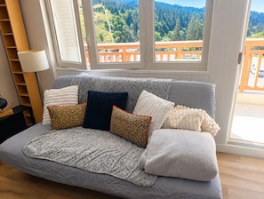 A cozy room with a grey sofa, a lamp, and a view of a forest through large windows. - Les Envols de Chamrousse - Proche Télécabines (Chamrousse)
