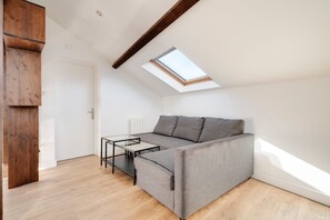 A modern loft apartment with a sloped ceiling, a skylight, a grey sofa, and a glass coffee table. - Le Vivaldi - Proche de la Gare (Nancy)