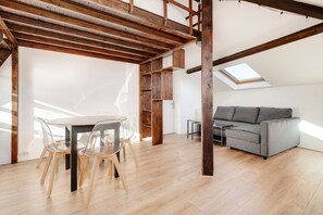 A spacious loft with a high ceiling, wooden beams, a skylight, a gray sofa, and a dining area with chairs. - Le Vivaldi - Proche de la Gare (Nancy)