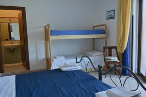 Una habitación con literas, una cama individual, una silla con cojín, una mesita y una ventana con cortinas.