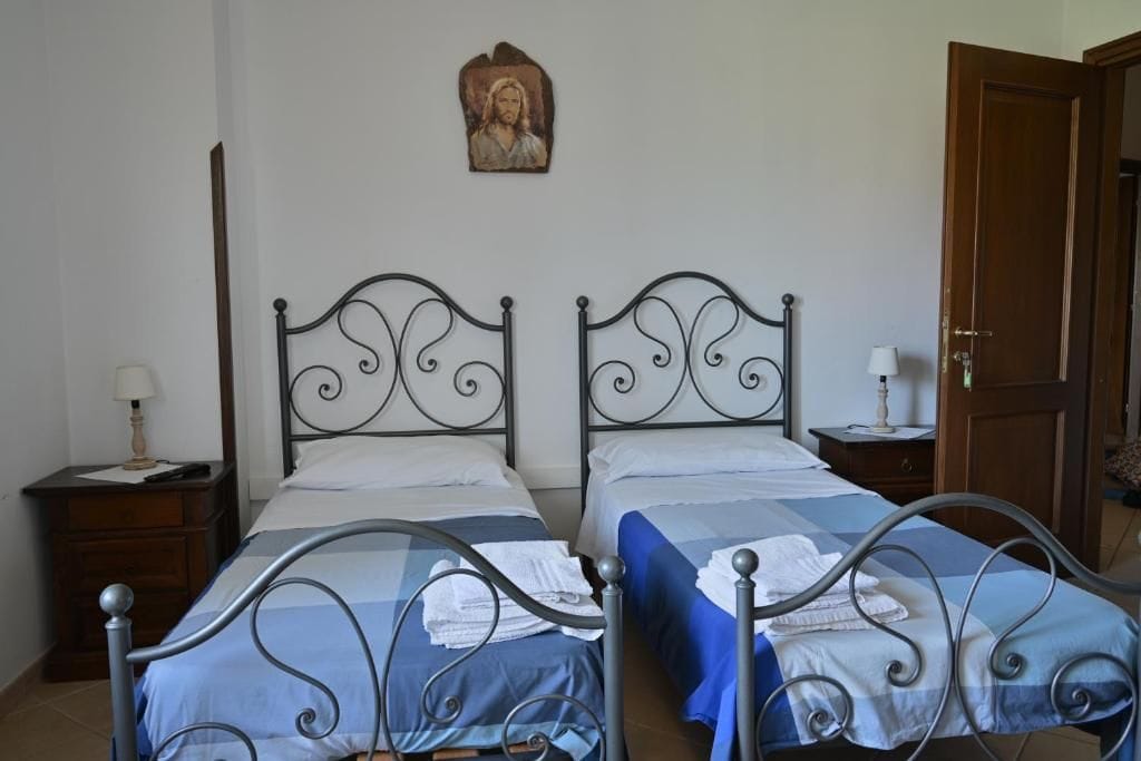 Une chambre avec deux lits à ossature métallique, une porte en bois et une petite table de chevet avec une lampe.