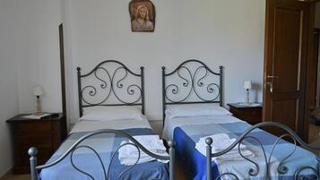 Une chambre avec deux lits à ossature métallique, une porte en bois et une petite table de chevet avec une lampe.