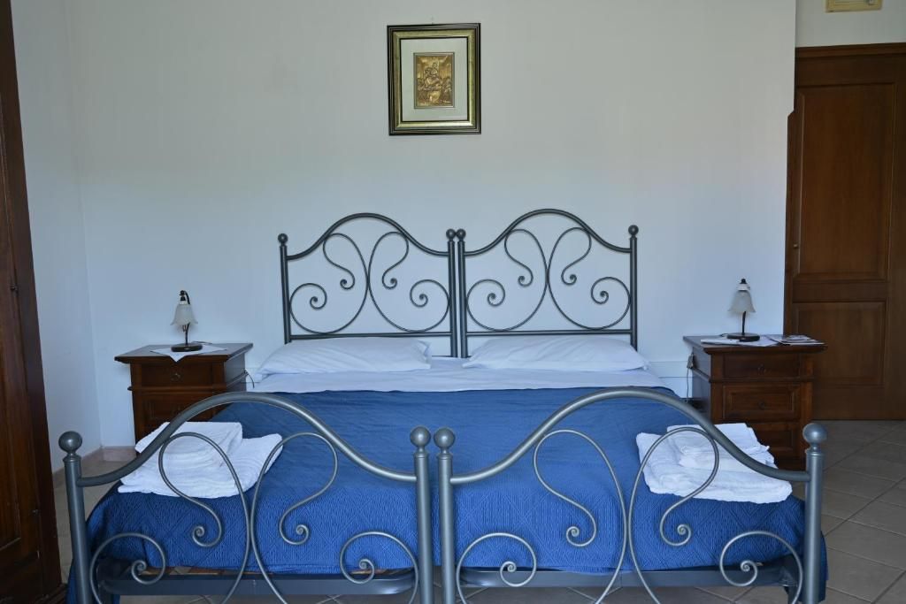 A bed with a metal frame, a blue bedspread, and white linens. There are two bedside tables with lamps.