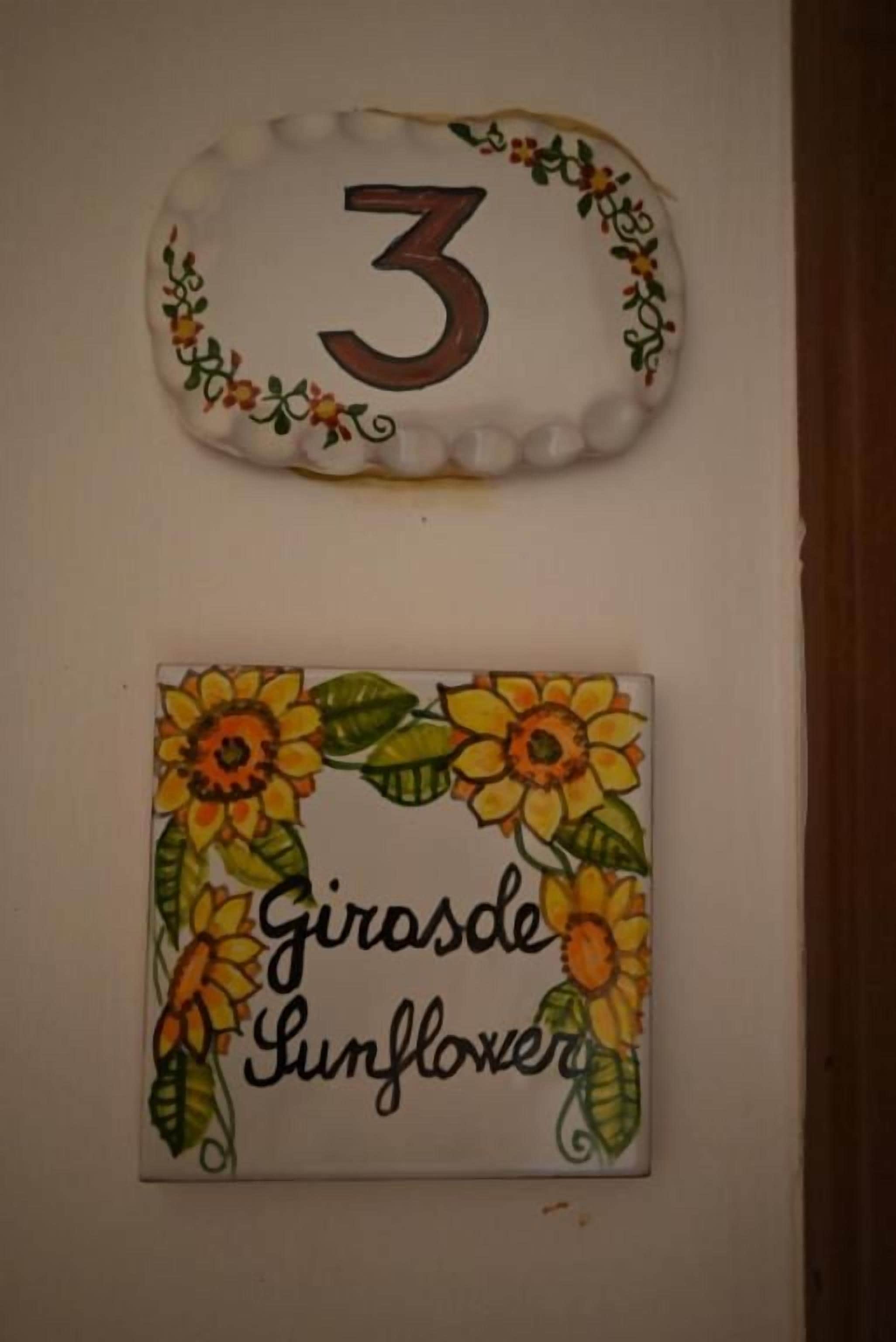 Dos adornos de pared: uno con el número 3 y otro con girasoles y el texto 'Girasde Sunflower'.