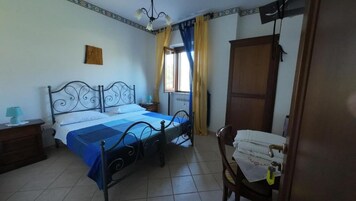 Un dormitorio con cama, mesita de noche, silla, armario y ventana con cortinas.