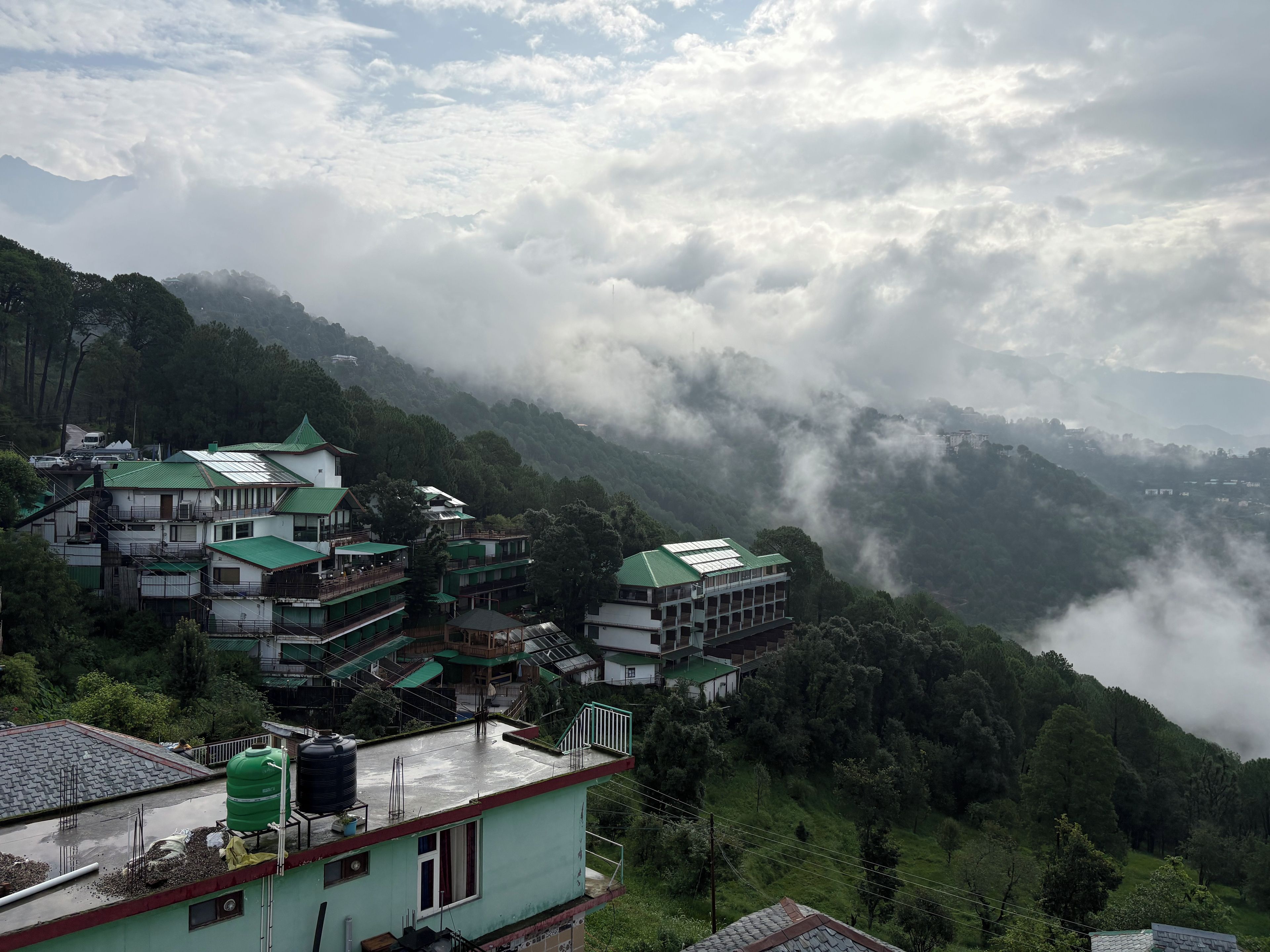 A mountainous village with traditional buildings, some with green roofs, and a valley shrouded in mist.