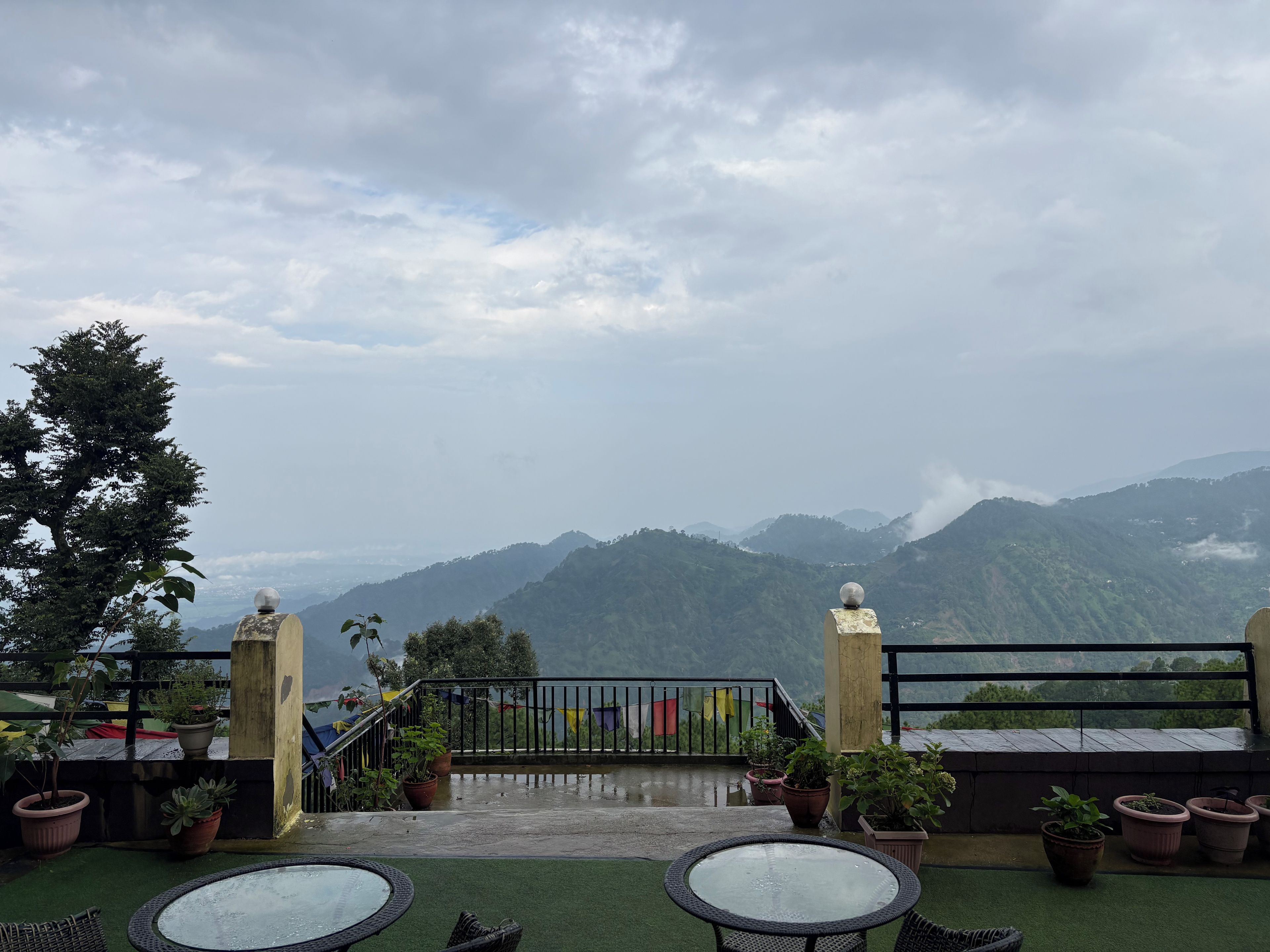 Una terraza con vistas a montañas, plantas en macetas y una barandilla.