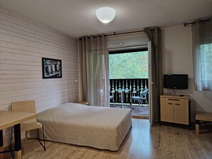 A room with a bed, a desk, a TV, and a balcony with a view of trees. - Studio with a swimming pool and views of the countryside (Ax-les-Thermes)