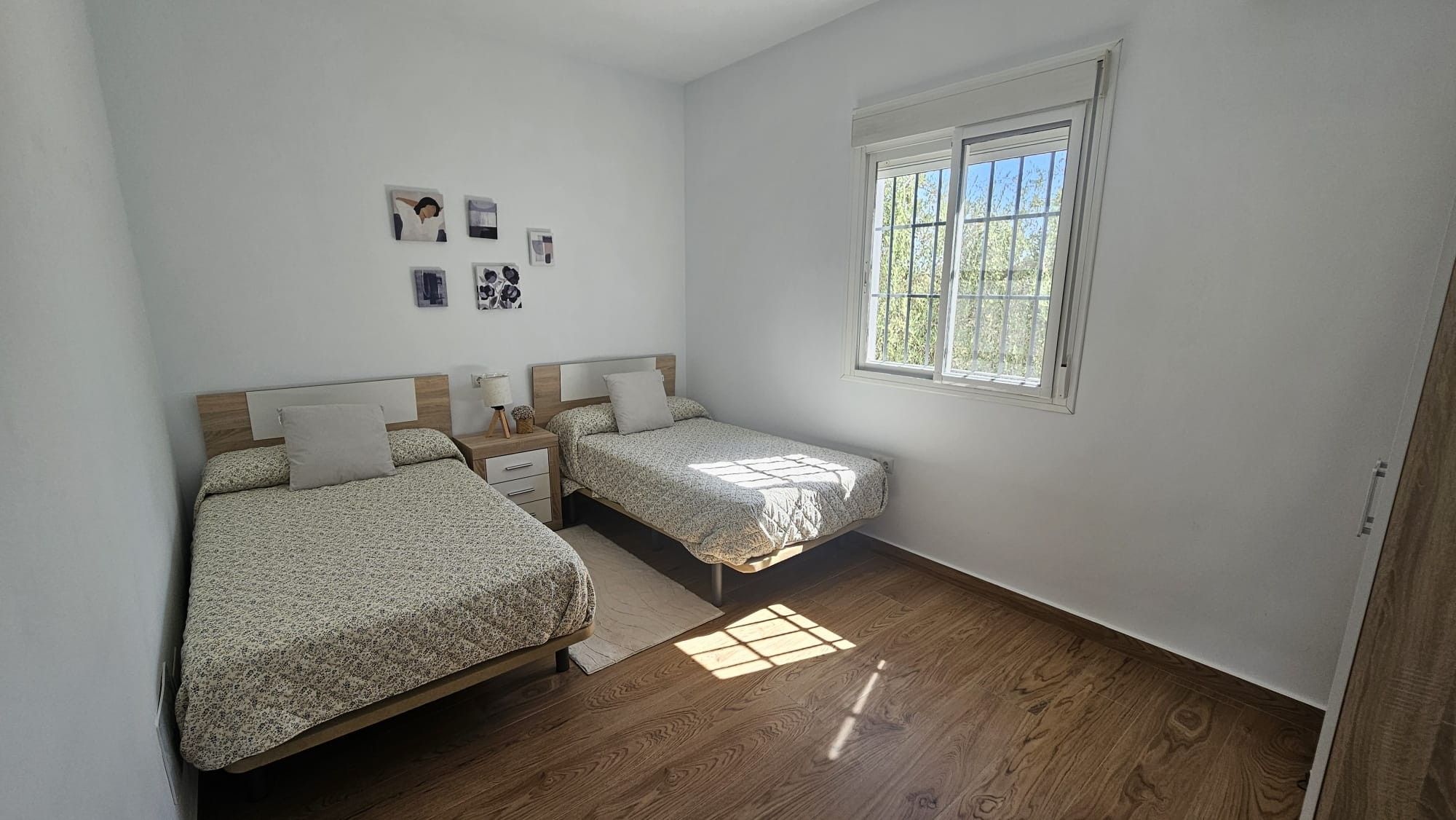 A bedroom with two beds, a window, and a small wall-mounted shelf with pictures.
