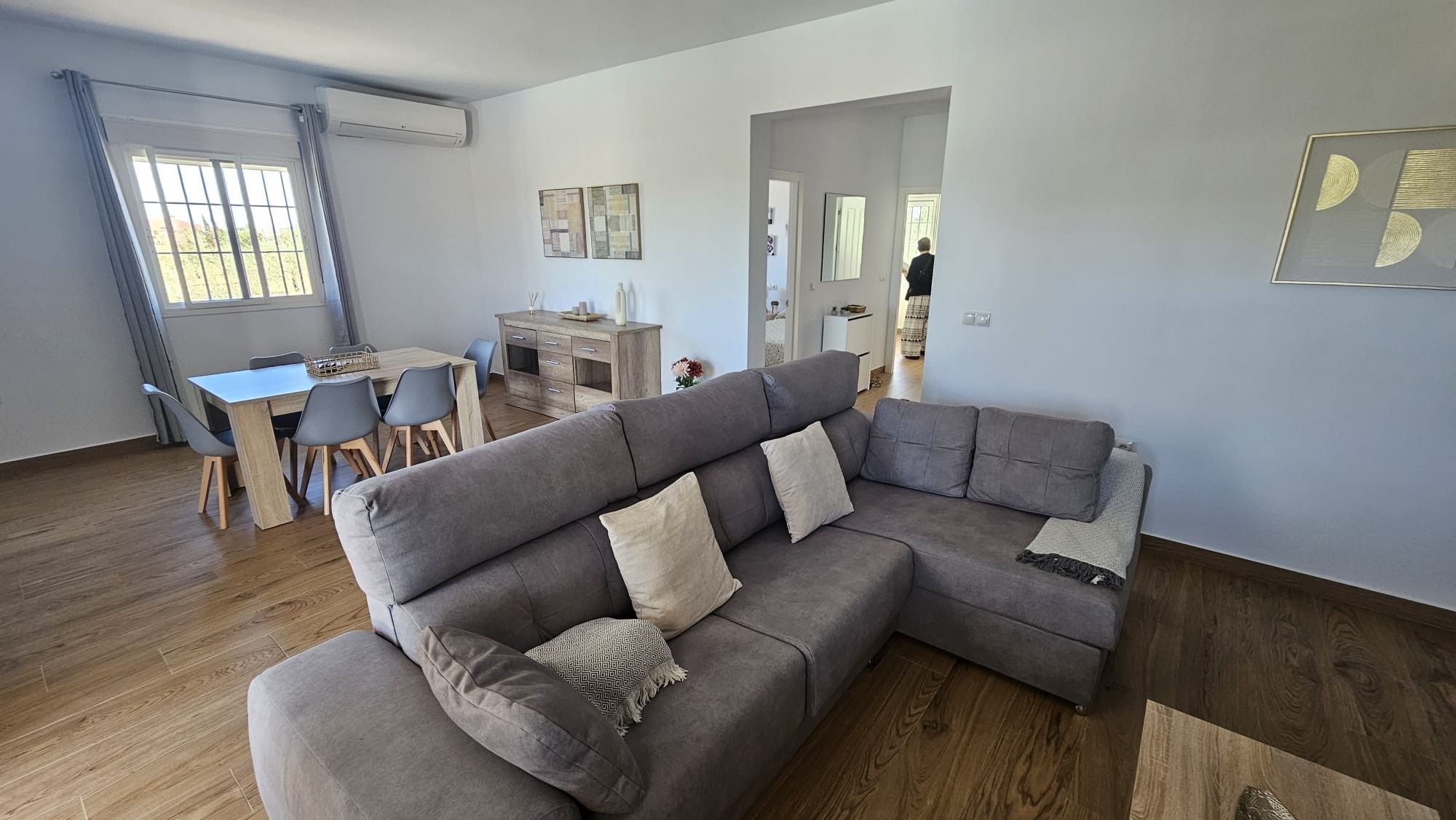 Una sala de estar moderna con un sofá modular, una mesa de comedor con sillas y una zona de cocina al fondo.